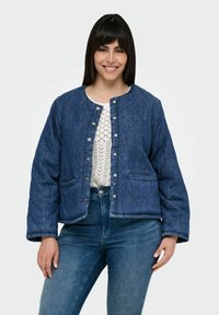 Jakna od wash denima sa stebnim uzorkom u tamnoplavoj boji, sa kopčama na dugmad, okruglim dekolteom i bočnim dzepovima; nosi se preko bijele pletene majice i plavih traperica.