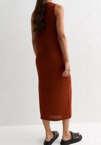 Abito midi senza maniche di colore ruggine con un motivo testurizzato ondulato, silhouette aderente e spacco laterale, abbinato a sandali neri.
