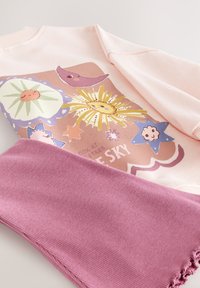 Sweat-shirt rose clair présentant des graphismes célestes colorés, associé à une écharpe rose côtelée, mettant en valeur des textures douces et des motifs ludiques.