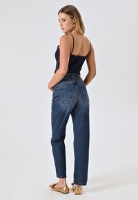 Top blu navy aderente con spalline sottili, abbinato a jeans in denim a vita alta e fit morbido. Scarpe flat dorate con dettaglio a fiocco completano il look.