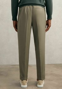 Pantalons beiges ajustés avec une coupe décontractée, taille élastique et ourlets retroussés, associés à des baskets de couleur claire.