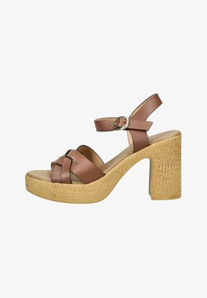 Brązowy skórzany sandał na wysokim obcasie z plecioną podeszwą na platformie i paskiem wokół kostki z srebrną klamrą, przedstawiony na białym tle.