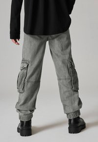 Grijze cargobroek met elastische boorden, zijzakken en een losse pasvorm. Gedragen met zwarte platformlaarzen en een lange zwarte shirt.