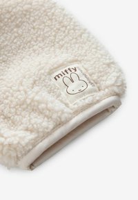 Tissu polaire doux de couleur crème avec un petit patch rectangulaire montrant le visage du lapin Miffy et le texte "miffy" en marron.