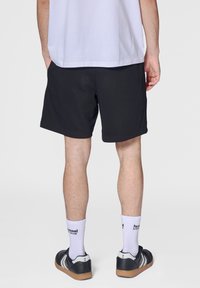 Schwarze Sportshorts mit elastischem Bund und glatter Textur. Dazu werden weiße Socken und schwarze Turnschuhe getragen.