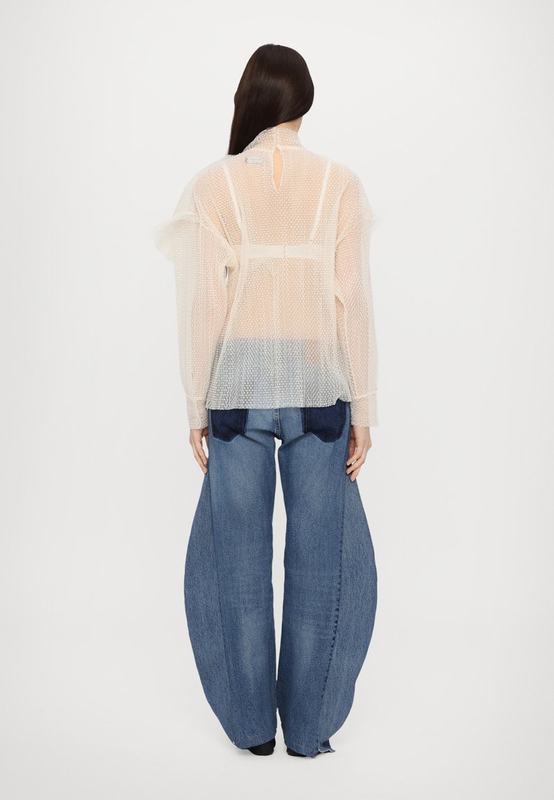 Gennemsigtig, mesh langærmet top i lys beige med en rund krave og nøglehul-detail på ryggen; samt brede blå denim jeans.