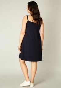Marineblauwe mouwloze jurk met een ontspannen pasvorm, voorzien van verstelbare bandjes en een zachte textuur, gecombineerd met witte sneakers.