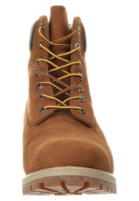 Botte en daim marron avec lacets jaunes et bordeaux, œillets métalliques, col rembourré et semelle épaisse et robuste.