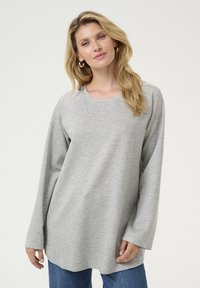 Tricou gri cu mânecă lungă, decolteu rotund, croială lejeră și textură netedă. Asortat cu blugi albaștri, expus pe un fundal alb.