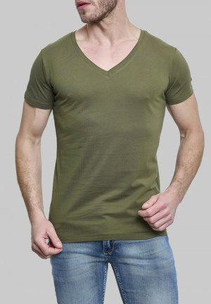 T-shirt vert olive à col en V en coton doux et élastique. Présente des manches courtes et une coupe ajustée, associé à un jean bleu.