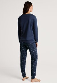 Marineblauwe longsleeve top gecombineerd met marineblauwe pyjamabroek met een sterrenpatroon. Glad materiaal, ontspannen pasvorm, ribgebreide manchetten op de top.