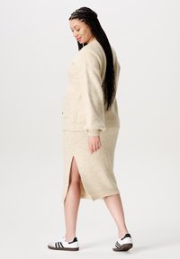 Gebreide beige trui en rok set, met een zijsplit op de rok en een relaxte pasvorm. Gestyled met witte sneakers met zwarte accenten.