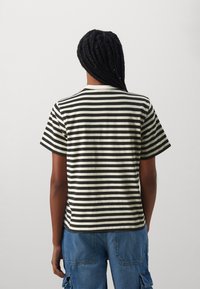 T-shirt en coton avec des rayures horizontales noires et crème, col rond, manches courtes et coupe décontractée, porté avec un pantalon cargo bleu.