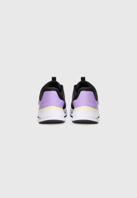 Een paar zwart en paarse sportschoenen met witte zolen, gezien vanuit de achterkant tegen een effen grijze achtergrond.