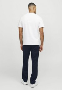 T-shirt en coton blanc à manches courtes, associé à un pantalon navy décontracté. Le tissu semble lisse ; les chaussures sont de style athlétique blanc.