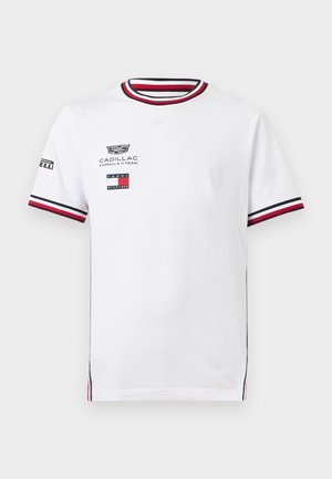 T-shirt blanc à manches courtes avec col rond et poignets de manches rayés rouge, noir et blanc, logos Cadillac et Tommy Hilfiger à l'avant.