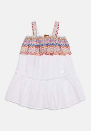 Robe blanche sans manches avec un motif zigzag multicolore sur un corsage froncé et des bretelles, avec une petite décoration argentée près du bas.