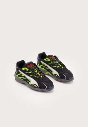 Paar schwarze und neongrüne Sportschuhe mit Flammenmustern, weißen Seitenstreifen und rotem Markenlogo auf der Zunge, auf weißem Hintergrund dargestellt.