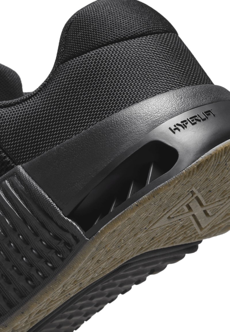 Zwarte sportieve schoen met een bovenkant van textuurstof, rubberen zool met een licht patroon en de zichtbare merknaam "HYPERLIFT" aan de zijkant.