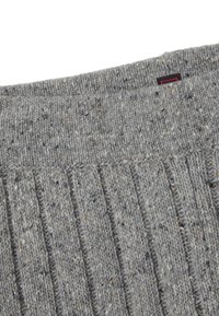 Tejido de suéter de punto gris con una textura acanalada. Presenta pequeñas motas de un color más claro y una etiqueta negra con acentos rojos en el cuello.