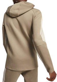 Sudadera con capucha en beige de textura suave. Presenta paneles laterales blancos en contraste y un ajuste relajado, vista desde la parte posterior.