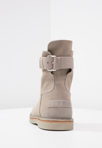 Grå mockaankelboots med spänndetalj, rundad tå och beige gummisula, med en logotyp på hälen.