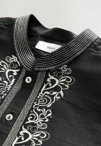 Black shirt with a mandarin collar, featuring silver embroidered floral patterns and button placket; smooth texture with contrast stitching detail.