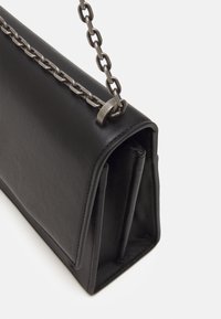 Svart läderhandväska med en strukturerad form, silverkedja som axelrem och framträdande dragkedjedetalj på sidan. Slät textur och minimalistisk design.
