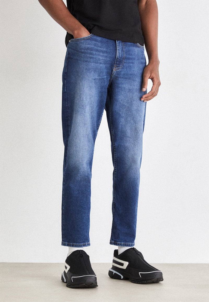 Modré džíny z denimu s rovný střih, s vybledlým vzhledem a klasickým pětipocket designem, doplněné černými teniskami na zip.