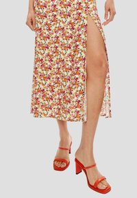 Falda midi floral de tela blanca con flores de colores, con una abertura en el lado. Combinada con sandalias de tacón rojas con tiras.