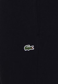 Svart bomullstyg med en liten grön och vit broderad krokodil-logotyp. Slät textur med en figurnära design.