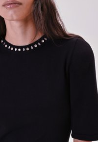 Top lavorato a maglia nero con scollatura rotonda decorata con embellishments metallici e riflettenti. Maniche corte e design aderente.