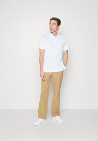 Weißes Polohemd mit Zweiknopf-Leiste, khakifarbene Hose und weiße Sneakers. Glatter Stoff, bequemer Schnitt und maßgeschneiderter Look.