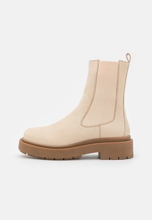 Botte Chelsea en cuir beige avec panneaux latéraux élastiques, languette de tirage et semelle épaisse à crampons marron.