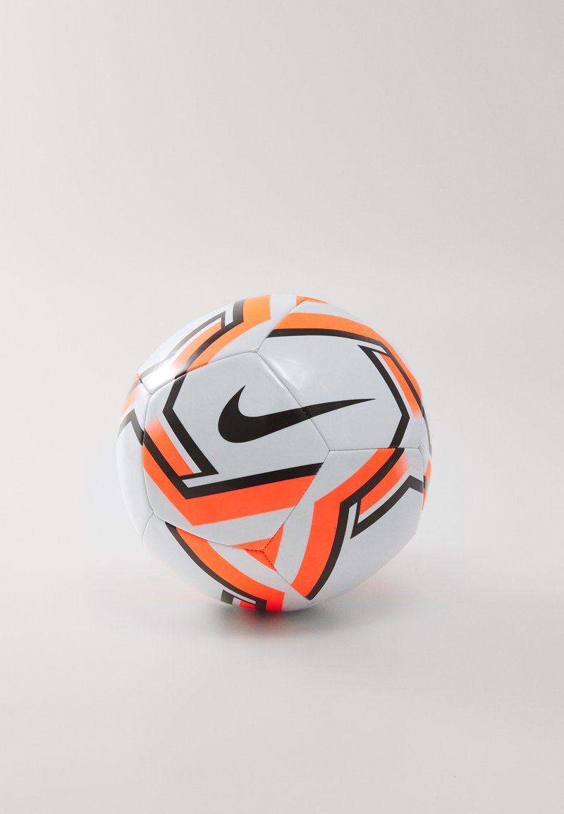 Bela nogometna žoga z oranžnimi in črnimi geometrijskimi vzorci, ki ima izstopajoče črno Nike logo, gladko površino in šivane panele.