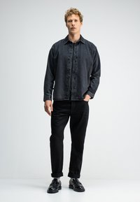 Zwarte denim overhemd met knoopsluiting aan de voorkant, lange mouwen en een ontspannen pasvorm. Gecombineerd met zwarte broeken en leren schoenen.