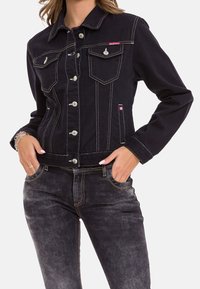 Schwarze Denimjacke mit silberner Hardware, kontrastierenden Nähten, zwei Brusttaschen und einer taillierten Passform, kombiniert mit verwaschenen schwarzen Jeans.