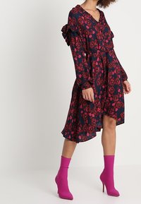 Vestido floral en azul marino con flores rojas, mangas con volantes, escote en V y un dobladillo fluido. Combinado con botas de tobillo rosas.