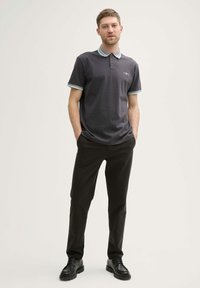 Polo de color gris oscuro con tejido texturizado, de manga corta y con ribete azul claro. Combinado con pantalones negros y zapatos negros.