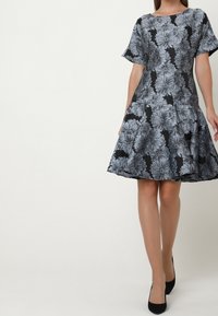Krátký rukáv šaty v černé barvě s květinovým vzorem v odstínech šedé, s rozšířenou siluetou a lodičkovým výstřihem.