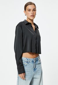 Camisa negra corta hecha de tela suave, con cuello puntiagudo y cierre de botones, combinada con jeans de cintura alta en azul claro.