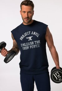 Hihaton tummansininen collegepaita, jossa lukee "PROJECT ANVIL UNLEASH THE IRON POWER". Kangas on pehmeä ja malli on rento. Paita on käytössä painonnostotankojen kanssa.