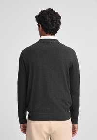 Maglione grigio scuro a maglia con scollatura rotonda, polsini e fondo a coste, caratterizzato da una superficie liscia e un design semplice.