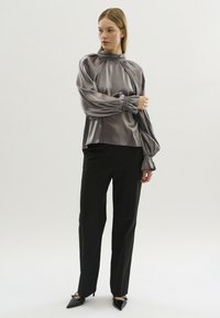 Zijdeachtige, grijze blouse met gathered mouwen en hoge halslijn, gecombineerd met zwarte rechttoe rechtaan broeken en zwartpuntige hakken.