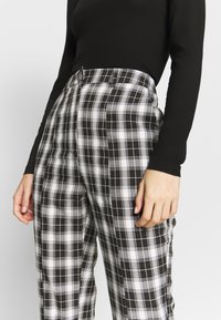 Svart långärmad topp i kombination med högmidjade rutiga byxor i svart och vitt, med ett rutig mönster och sidofickor.