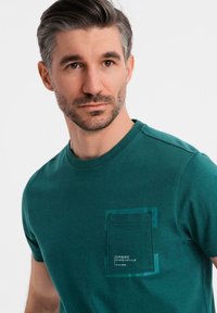 Mörkgrön bomulls T-shirt med en bröstficka med kontrasterande kant och tryckt logotyp, klassisk rund halsringning och korta ärmar.