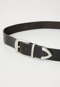 Cinturón de cuero negro con una hebilla rectangular plateada y un extremo puntiagudo distintivo. Cuenta con múltiples agujeros de ajuste para el tamaño.