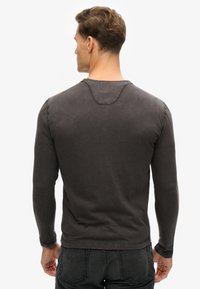 Dunkelgraues Langarmshirt aus weichem Stoff. Verfügt über einen runden Ausschnitt und gerippte Bündchen. Einfaches, lässiges Design mit minimalen Nahtdetails.