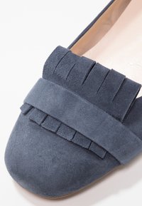 Scarpa piatta in suede blu navy scuro caratterizzata da una fascia larga con accenti plissettati e una punta arrotondata liscia. L'interno è morbido con cuciture minime.
