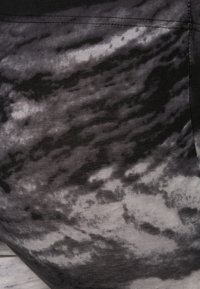 Gros plan d'un tissu noir et gris avec un motif ondulé ressemblant à des nuages et des coutures visibles le long du bord supérieur.